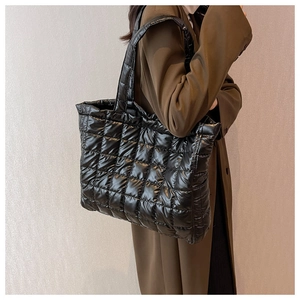 Detail of a black quilted puffer tote bag in shiny nylon worn over an olive green trench coat