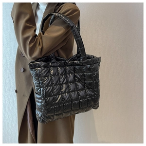 Close-up of black quilted puffer tote bag worn by a model in a wool coat for autumn styling