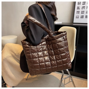 Deep brown quilted puffer tote bag shown on shoulder in a modern indoor setting