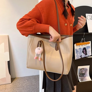 Minimalist cream tote bag with dark brown trim and cute plush monster charm on shoulder