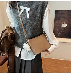 Detailaufnahme der khakifarbenen Beuteltasche mit Markenschriftzug und Anhänger