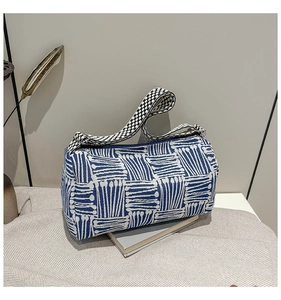 Detailed view of blue and white striped cylindrical bag with woven wide shoulder strap