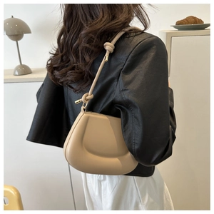 Détail du sac beige incurvé avec bandoulière nouée et finitions métalliques dorées