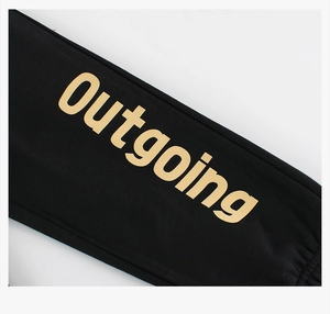 Detail of children's cotton sweatpants featuring golden Outgoing letter print on black fabric