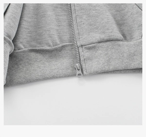 Detail showing the metal zipper head and ribbed hem on a grey zip-up hoodie