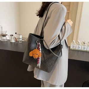 Detail der schwarzen Shopper-Tasche aus Kunstleder mit Hunde-Plüschanhänger und Quaste