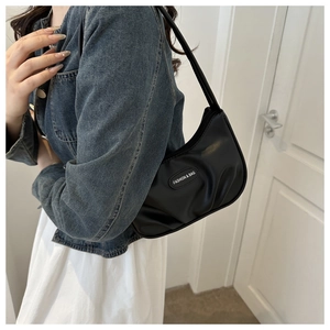 Detail of black pleated crescent shoulder bag featuring a fashion logo label and soft texture