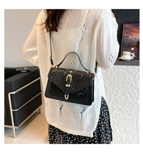 Detail showing snake pattern embossed flap and gold lock on elegant black crossbody bag