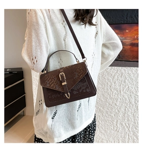 Detail of snake skin texture and metal lock on a brown crossbody bag worn by model