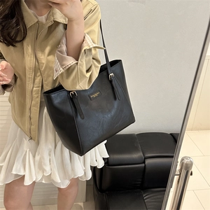 Classic black leather tote bag with gold logo and adjustable straps on a model