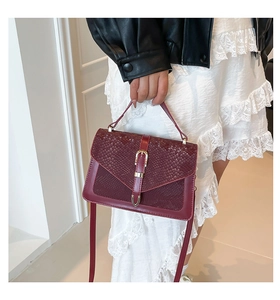 Detail of burgundy handbag with snake pattern texture and gold buckle on a model