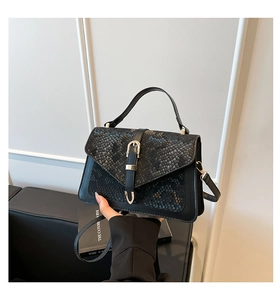 Close-up of black handbag featuring snakeskin texture and gold U-shaped buckle detail