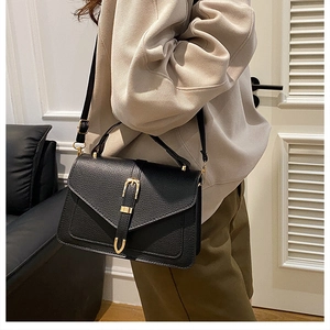 Detail of black pebbled leather handbag with V-shaped flap and gold metal buckle