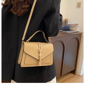 Close-up of khaki textured leather shoulder bag with gold hardware worn by a model