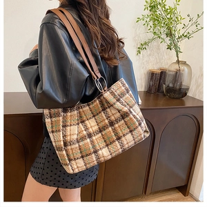 Detail of plaid tote bag with leather straps and metal rings in a cozy home setting