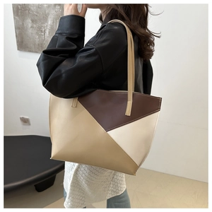 Detail of a geometric patchwork tote bag with brown and beige panels in an indoor setting
