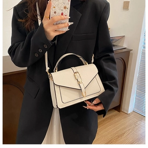Detail of cream leather crossbody bag with gold U-shaped buckle on a model