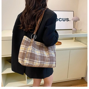 Detail of plaid tote bag with leather straps and metal rings shown on model