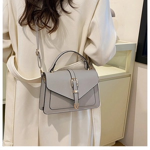 Minimalist grey faux leather crossbody bag with gold U-buckle worn by a model