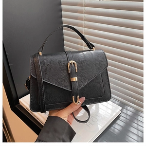 Detail of a black lychee-textured leather handbag with a gold buckle and top handle