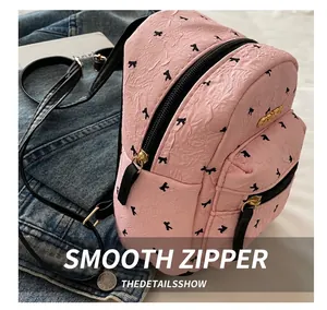 Detail of pink mini backpack featuring bow prints and smooth golden zippers on fabric