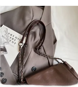 Detail van donkerbruine draagtas met metalen ketting op een grijze blazer