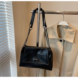 Detail van een zwarte leren shopper met kettingriem en metalen logo op een beige trenchcoat