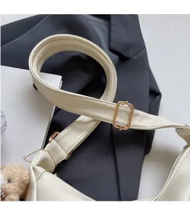Detail view of adjustable strap on beige crossbody bag with gold metal buckle and bear charm