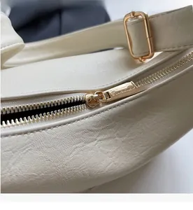 Close-up of smooth light gold metal zipper on cream leather crossbody bag texture