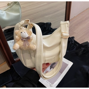 Detail of creamy white dumpling bag with pleated faux leather texture and bear charm