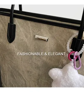 Detail of khaki textured tote bag with black leather trim and soft white plush charm