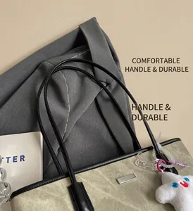 Close-up of beige canvas tote bag featuring black leather handles and silver logo detail