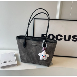 Detail of grey suede tote bag with black trim and a star plush charm accessory