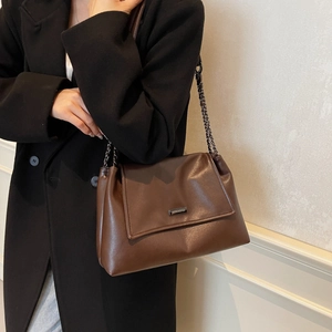 Bruine vintage kunstlederen shopper met metalen ketting over een zwarte jas