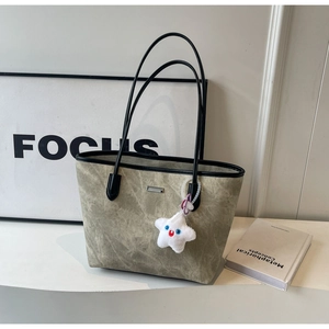 Detail of grey-green tote bag featuring a white star plush charm and a metal logo plaque