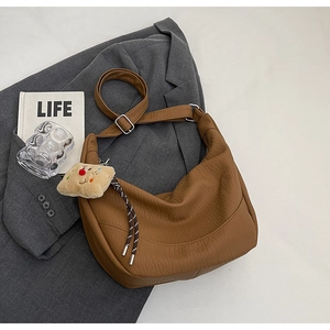 Detailed view of brown litchi pattern hobo bag with teddy bear charm on grey blazer