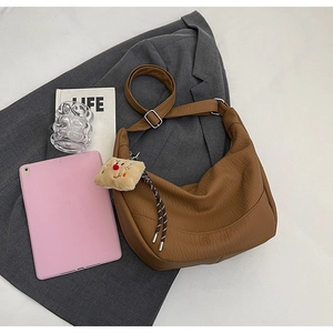 Detail of brown leather moon bag with textured litchi pattern and plush pendant charm