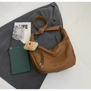 Detail of caramel faux leather dumpling bag with adjustable strap and plush charm