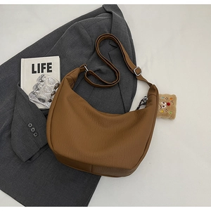 Detailed texture of brown leather crossbody bag with adjustable strap and plush charm