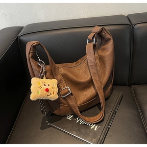 Detailed texture of brown litchi pattern PU leather bag with a plush smile charm
