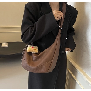 Detail of a brown half-moon hobo bag with a cute plush bear charm on a black coat