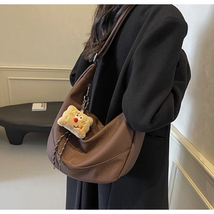 Detail view of a large brown moon bag with lychee grain texture and plush charm