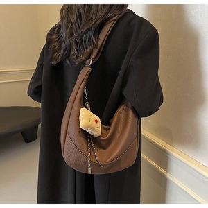 Brown leather crescent crossbody bag shown from behind featuring a cute bear keychain charm