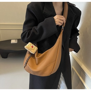 Close-up of brown crescent crossbody bag with lychee grain texture and plush charm