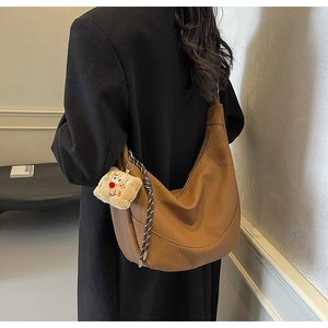Detail of brown pebbled leather hobo bag with plush charm and braided strap on model