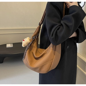 Detailed texture of brown leather crescent bag with cute plush pendant on black coat