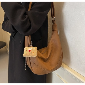 Brown lychee texture leather crescent bag with cute plush pendant shown on shoulder