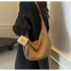 Brown litchi texture hobo bag with plush charm shown from a side-back view on model