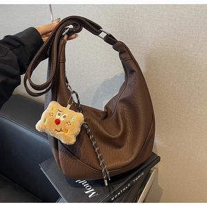 Detail view of large dark brown crescent bag with grainy leather and cute plush charm