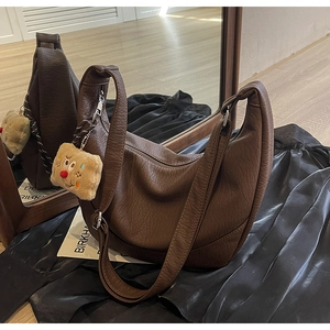 Detail view of dark brown pebbled leather hobo bag with playful plush charm on dark fabric